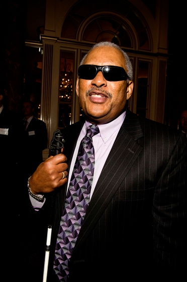 Dean posing for a photo, wearing a suit and sunglasses and holding a cane